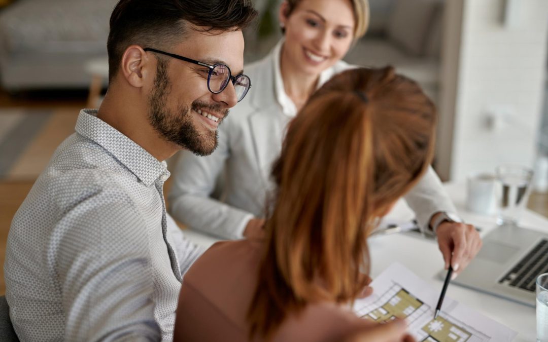 Three people smiling and discussing floor plans at a table with documents and a laptop.